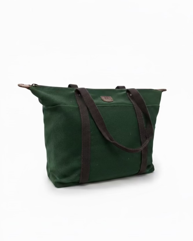An olive green canvas tote bag with dark brown webbed handles and a small metal logo plaque, displayed on a wooden table inside a retail store.