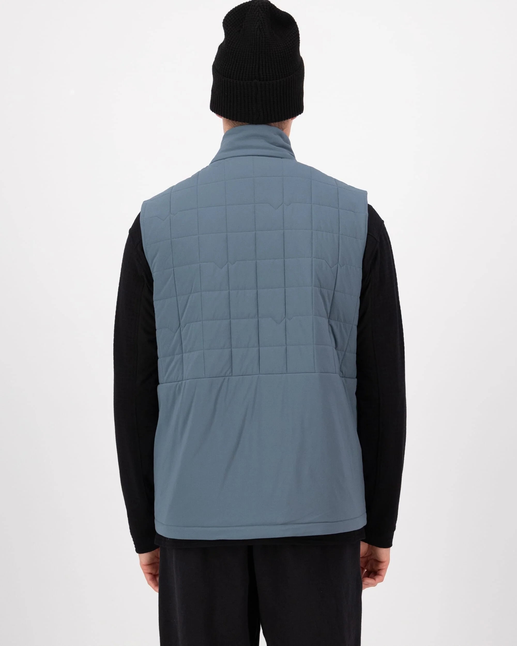 Person wearing a blue quilted vest over a black long-sleeve shirt on a white background