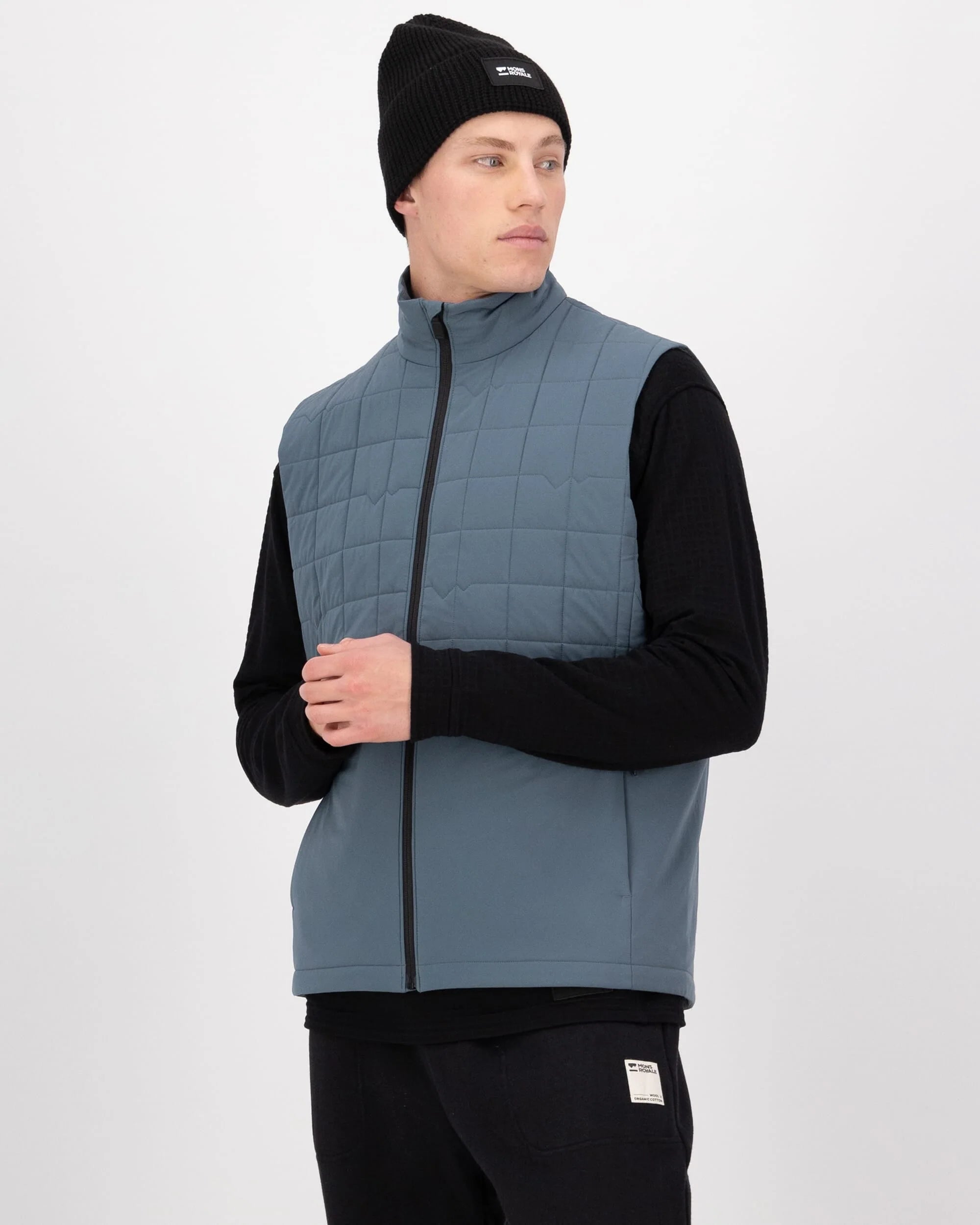 Man wearing a blue quilted vest over a black long-sleeve shirt on a white background