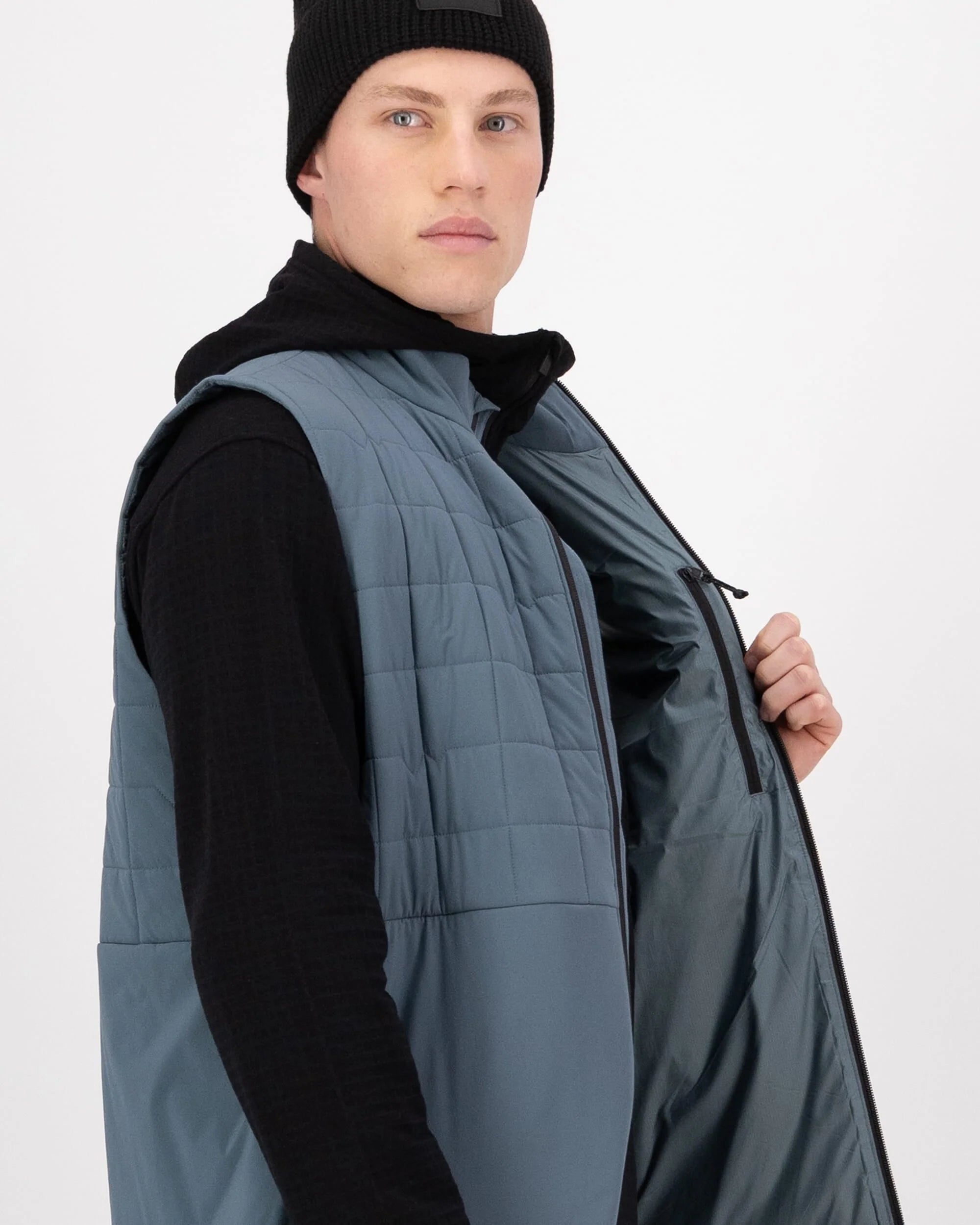 Person wearing a blue quilted vest over a black shirt on a white background