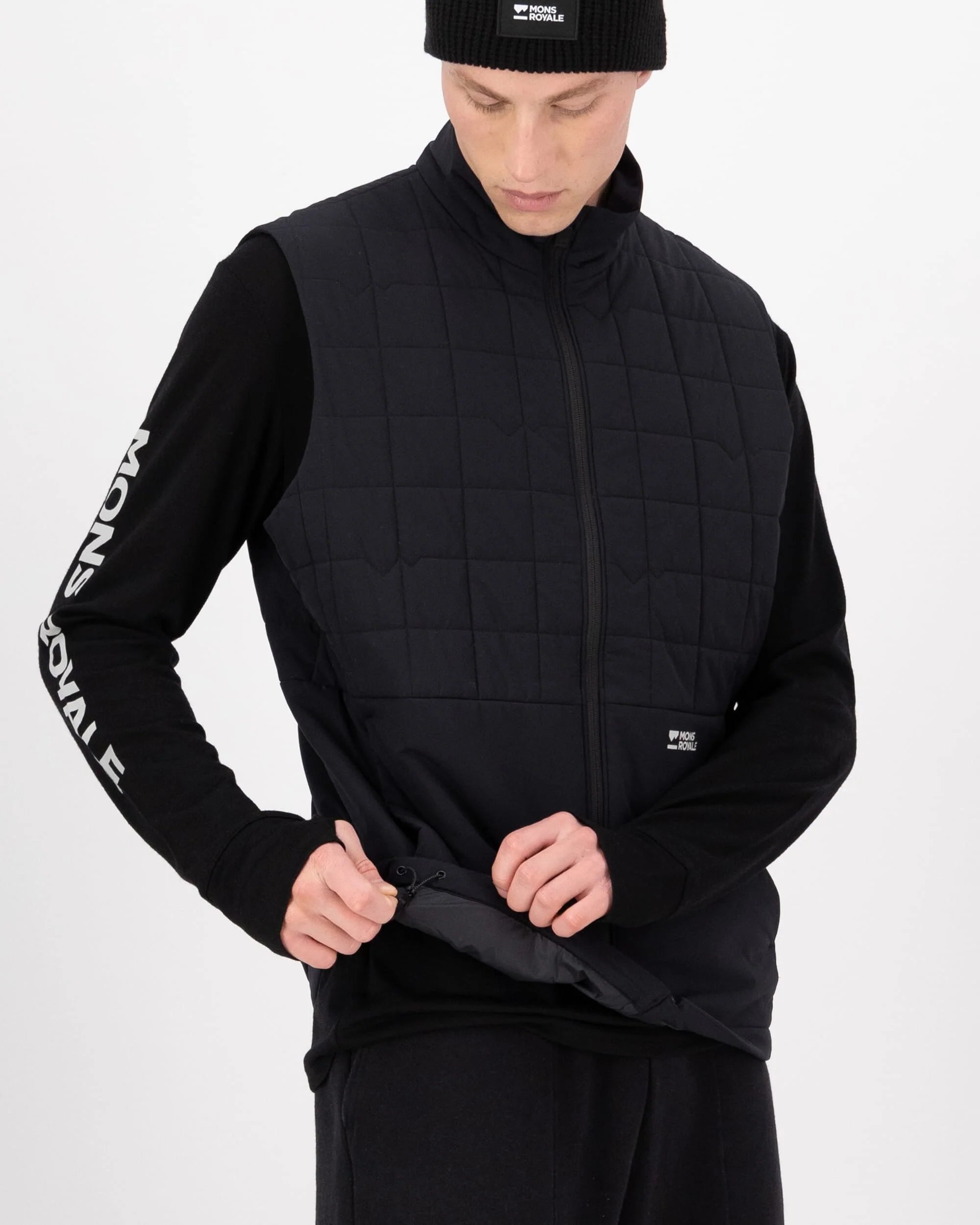 Person wearing a black quilted vest and black long-sleeve shirt with branding on a white background