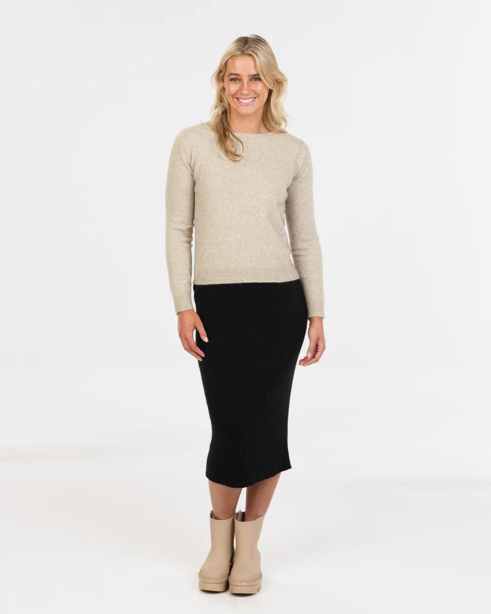 Woman wearing a beige sweater and black skirt on a white background