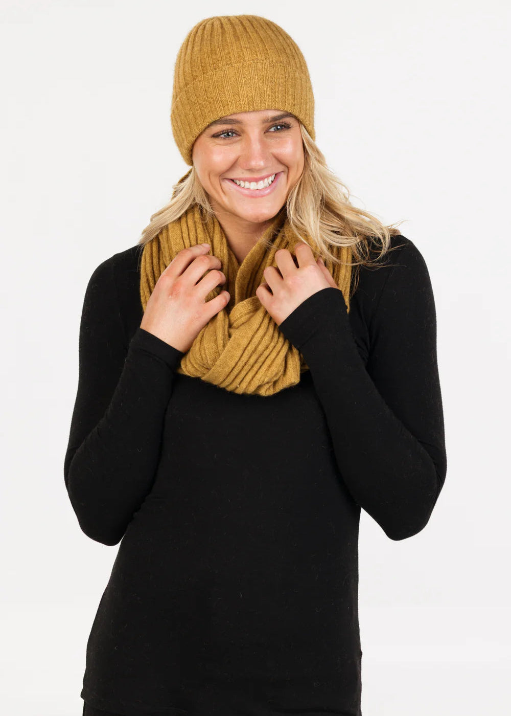 Woman wearing a marigold yellow knit beanie and scarf on a white background