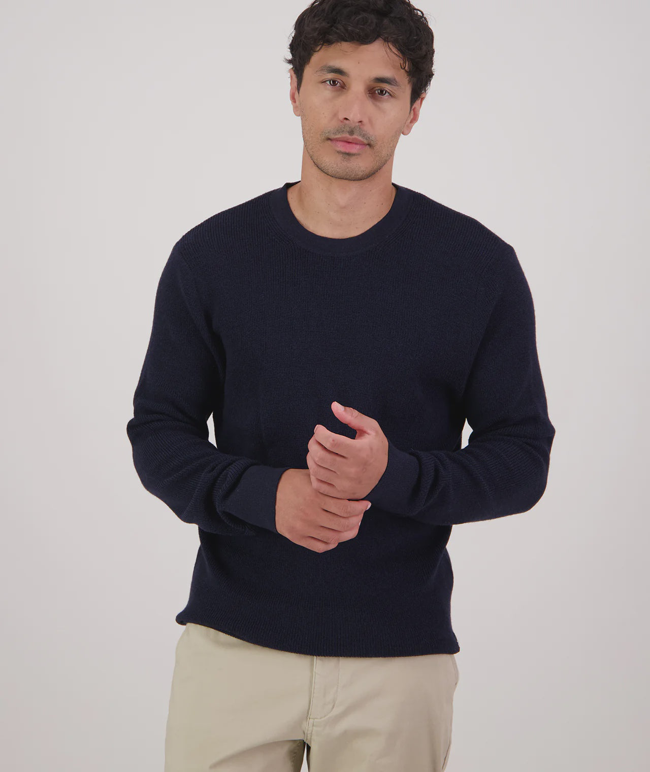 Man wearing a navy sweater and beige pants on a light gray background