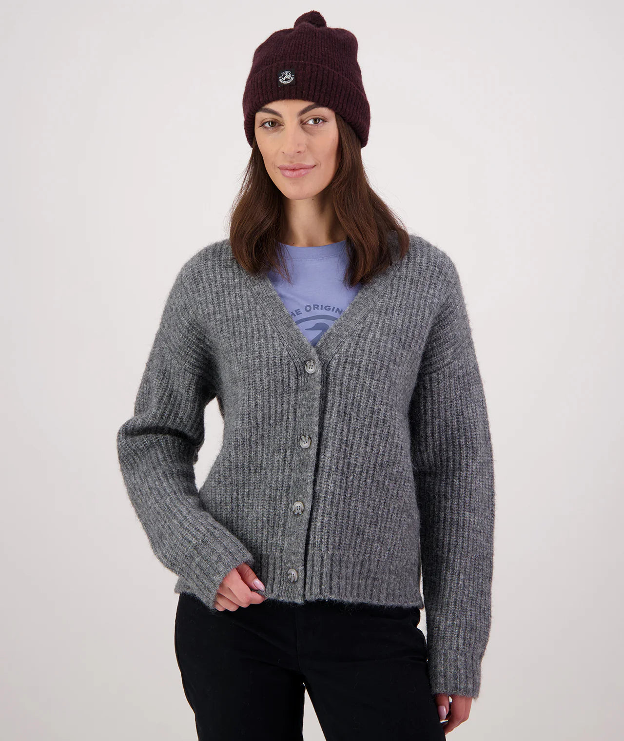 Woman wearing a gray cardigan, purple beanie, and black pants on a white background