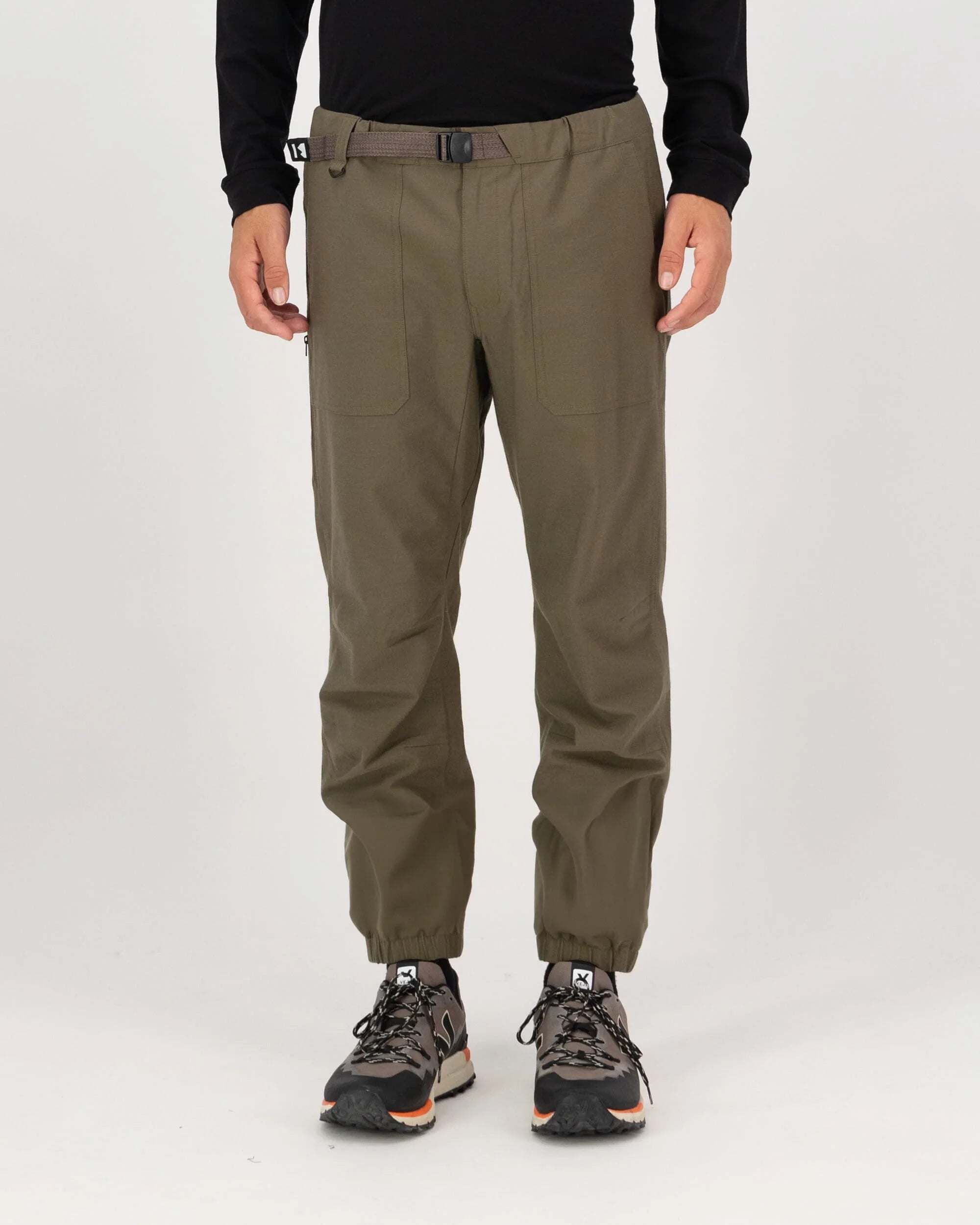 Person wearing olive green pants with a black top and hiking boots on a white background